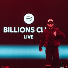 a man in black jacket and hat walking on stage with microphones behind him at billion's club live