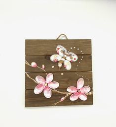 a wooden sign with pink flowers and butterflies painted on the wood, hanging on a white wall