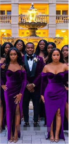 a group of people standing next to each other in front of a fountain wearing purple dresses