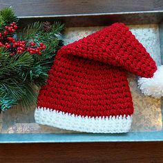 a red and white knitted santa hat sitting on top of a tray next to pine branches