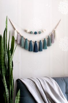 a wall hanging with tassels and beads on it next to a potted plant