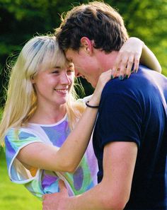 a young man and woman embracing each other in the middle of a grassy area with trees in the background