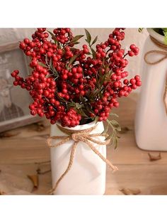 a white vase filled with red berries on top of a table