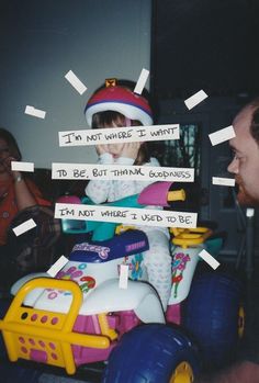 a young child sitting on top of a toy car with paper taped to it's sides