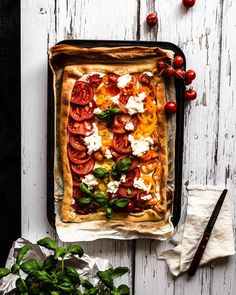 a person placing toppings on top of a pizza in a baking pan next to tomatoes and basil