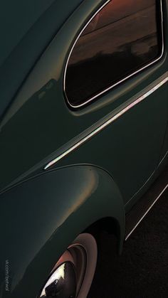 an old green car parked in a parking lot with the sun shining on it's side window