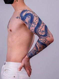 a man with a dragon tattoo on his arm and shoulder is wearing white pants, a black bandana and a baseball cap