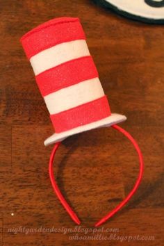 a red and white cat in the hat headband on a wooden table next to a clock