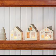 three lit candles are sitting on a shelf in front of a house and christmas tree