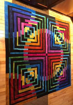 a colorful quilt hanging on the wall next to a wooden paneled wall with text that reads just in time i pattern by laurie shfrin and