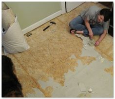 a woman sitting on the floor in front of a door with torn up walls and debris all around her