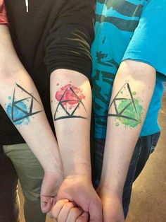 two people with matching tattoos on their arms holding each other's hands and looking at the camera