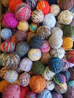 balls of multicolored yarn are piled on top of each other in a bin