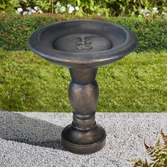 a metal pedestal sitting on top of a cement slab in front of some grass and bushes