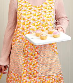 a woman in an apron holding a tray with cupcakes on it's side