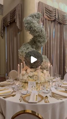 the table is set with white flowers and gold place settings for an elegant dinner party