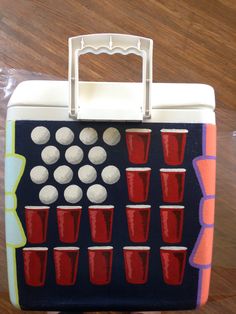 a lunch box with red and white cups on the side, sitting on top of a wooden table