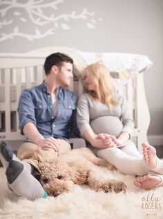 a man and woman sitting on a bed with a dog in their lap while the baby is laying down next to them