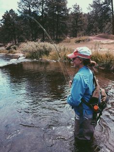 a man standing in the water while holding a fishing rod and wearing a red hat