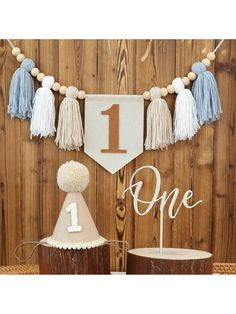 the first birthday banner with tassels is hanging on a wooden wall next to other decorations