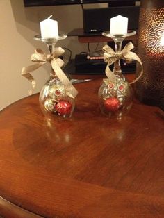 two glass candlesticks with bows and ornaments on top of a wooden table in front of a television