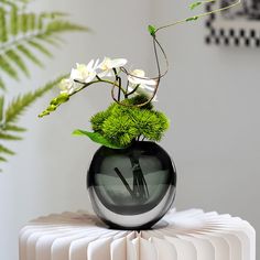 a vase filled with flowers on top of a white table next to a green plant