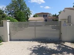 a gated driveway with gravel and trees in the back ground, next to a house