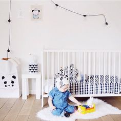 a baby sitting on the floor in front of a crib playing with a toy