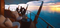 two people standing on the deck of a boat looking out over the ocean at sunset