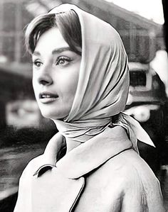 black and white photograph of a woman in a coat standing next to a train track