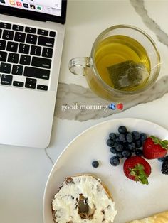 a white plate topped with fruit next to a cup of tea and a laptop computer