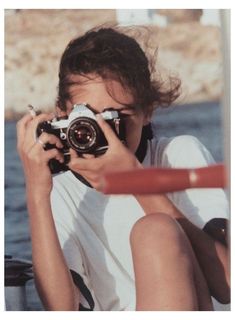 a woman holding a camera up to her face while sitting on a boat in the water