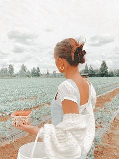 a woman in a white dress is holding a basket with carrots on it and looking at the field