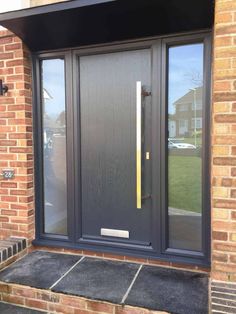 a grey front door with glass and yellow handle on the side walk in front of a brick building