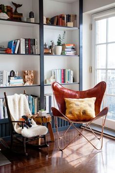 a living room filled with furniture and bookshelves next to a large window on top of a hard wood floor