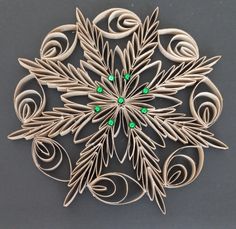 a paper snowflake with green beads on it's center and leaves in the middle