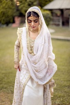 a woman in a white dress and headpiece is walking through the grass with her hands on her hips