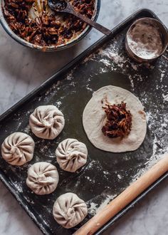 some dumplings are sitting on a baking sheet and next to a bowl of food