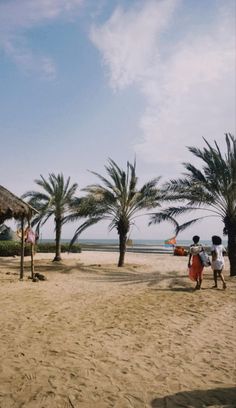 some people are walking on the sand near palm trees and an thatched roof hut