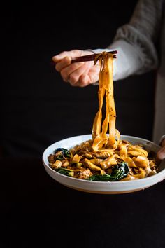 a person holding a bowl of noodles with chopsticks in their hand while eating it