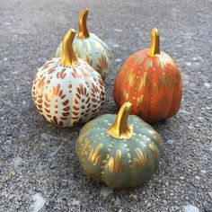 three painted pumpkins sitting on top of a cement ground next to each other in different colors