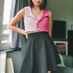 a woman standing in front of a window wearing a pink and white top with black pleated skirt