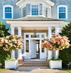 the front entrance of a house with white trim and pink flowers on the planters