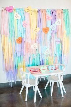 a table and chairs in front of a wall with colorful streamers hanging from it