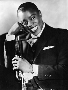 a black and white photo of a man in a suit smiling at the camera with his hand on his head