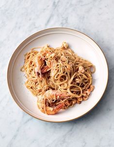 a white plate topped with pasta and shrimp on top of a marble countertop next to a fork