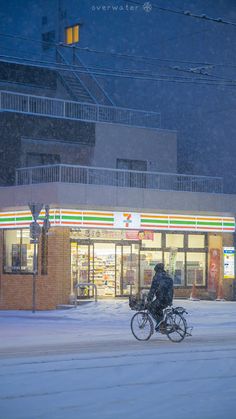 a man riding a bike down a snow covered street in front of a convenience store