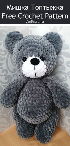 a gray teddy bear sitting on top of a wooden table next to a white wall