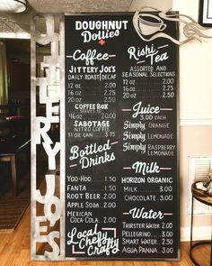 a menu board with drinks on it sitting in front of a table and chairs next to a wall