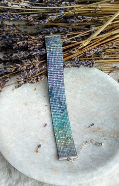 a piece of jewelry sitting on top of a white plate next to dried lavenders